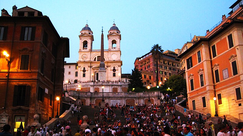 Praça na Roma com uma escada, igreja e diversas outras construções, repleto de pessoas