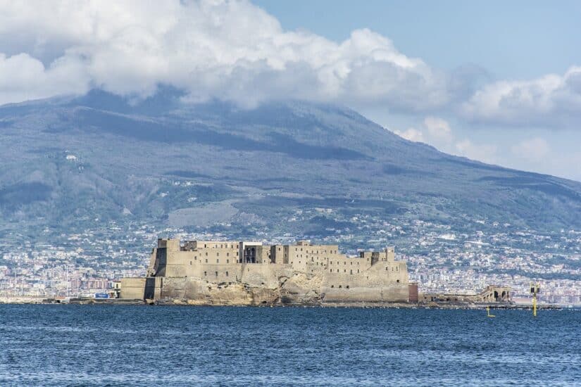 Castelo com vista para o mar e montanhas em Nápoles.