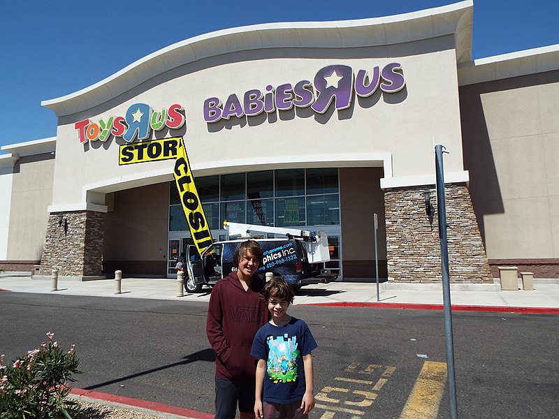 Loja com a placa Toys R-Us e babies r us e com duas crianças na frente