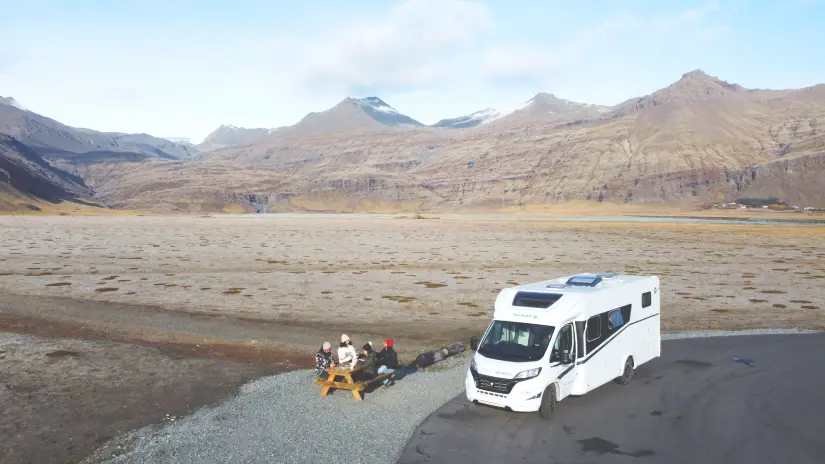 Motorhome na Islândia estacionado perto de uma mesa de piquenique, cercado por vastas montanhas rochosas sob um céu nublado.