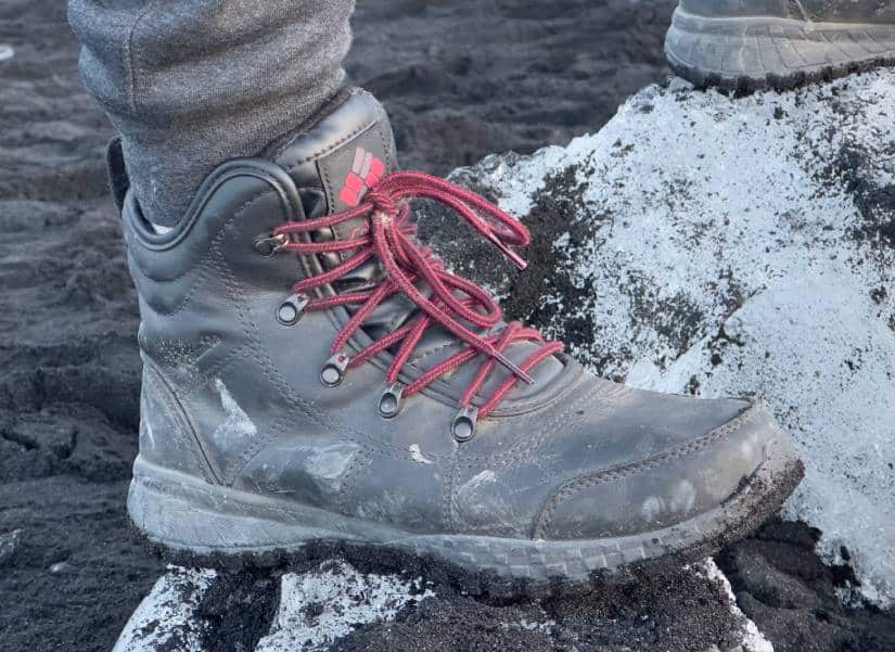 Uma bota de caminhada cinza com cadarços vermelhos está sobre uma superfície rochosa preta e branca.