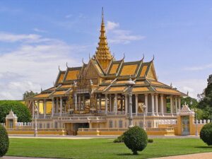 Templo com telhado dourado e torres intrincadas, emoldurado por um céu azul claro e vegetação exuberante.