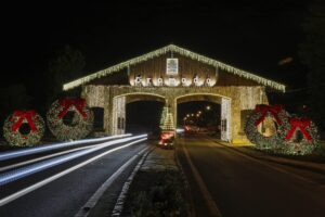 Portal em arco iluminado com luzes de Natal e guirlandas, com rastros de luz dos veículos que passam à noite.